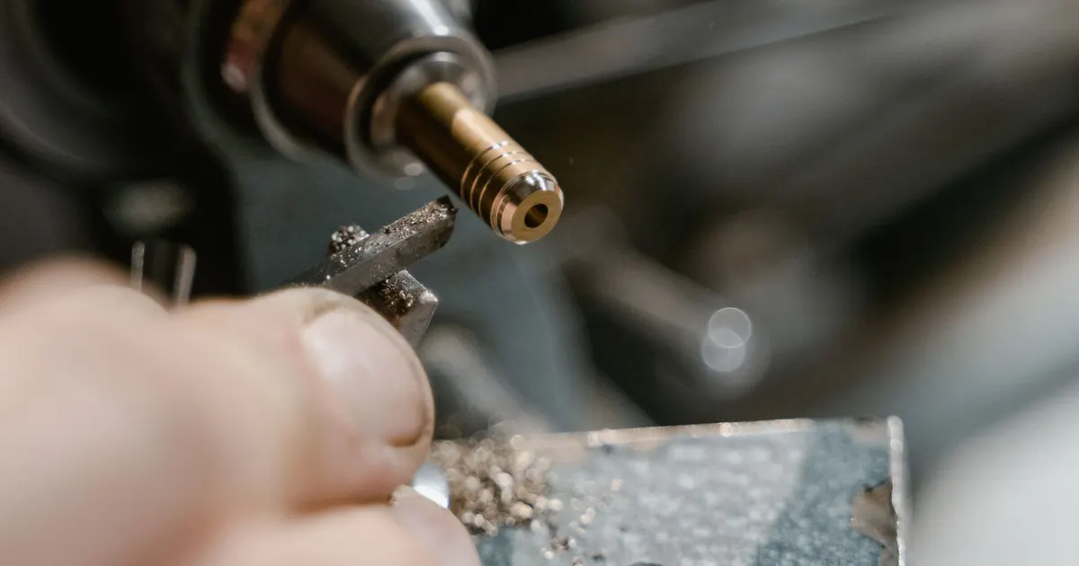 Hand holding a small machined metal part with fine machining swarf beside it, burr removal at the bench