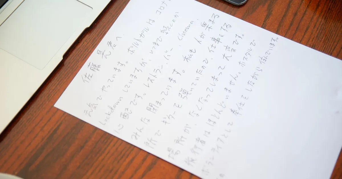 Handwritten Japanese note on white paper lying on a wooden desk, an example of Japanese text a shop must translate