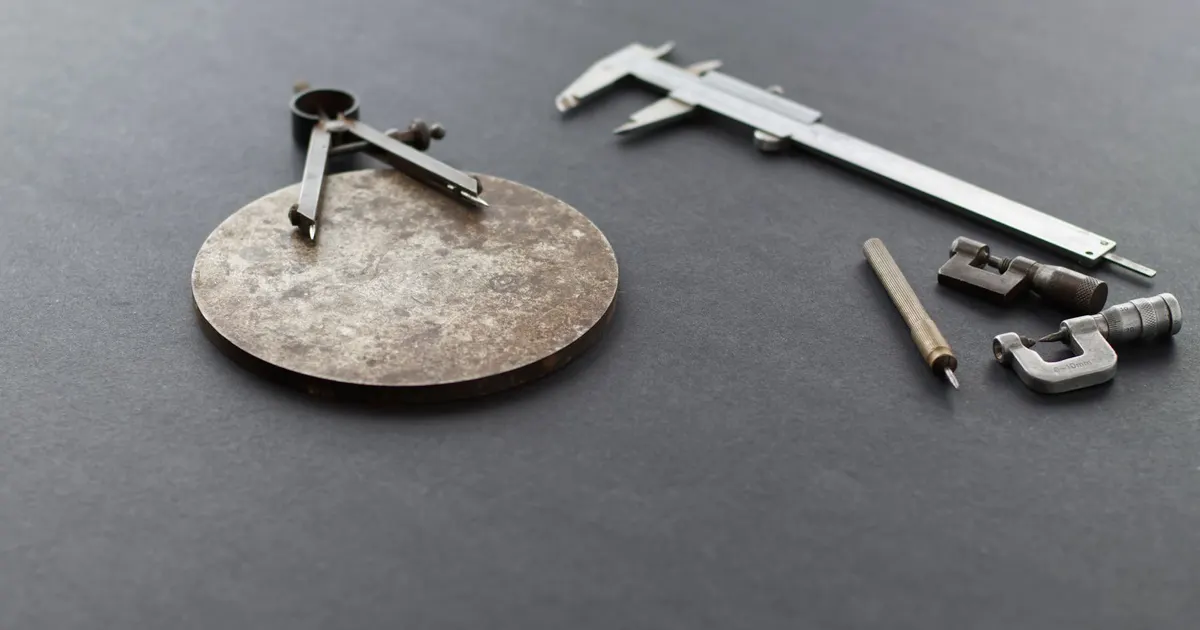 Vernier caliper, dividers and a metal disc on a dark surface, measuring tools used to check a JIS B 0401 fit