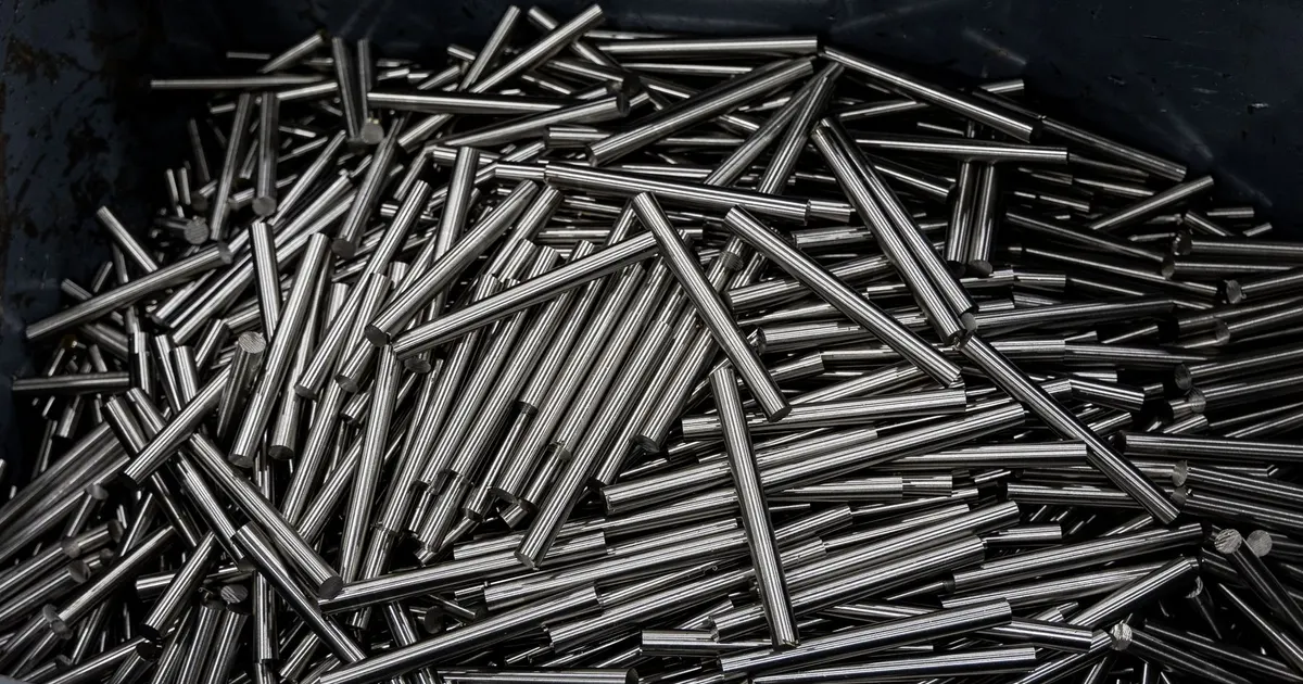 Pile of thin straight metal rods in a container, bar stock waiting to be cut and machined
