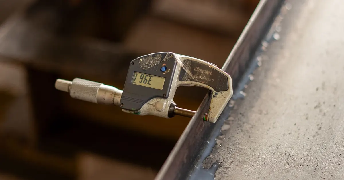 Digital micrometer measuring the thickness of a metal edge, the kind of measurement recorded in an inspection report