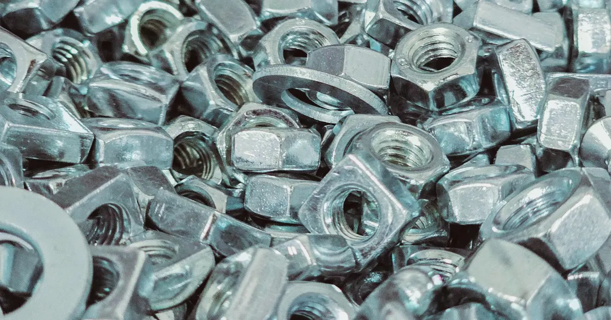 Heap of metal nuts and flat washers in a pile, simple turned ring shaped hardware similar to spacers and collars